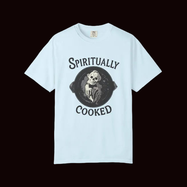A light blue short-sleeve crewneck t-shirt with a black graphic print on the front featuring a skeleton in a frying pan and the words 'SPIRITUALLY COOKED'.