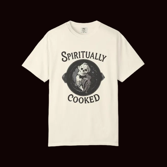 An off-white short-sleeve t-shirt with a black graphic print on the front featuring a skeleton in a frying pan and the text 'SPIRITUALLY COOKED'.