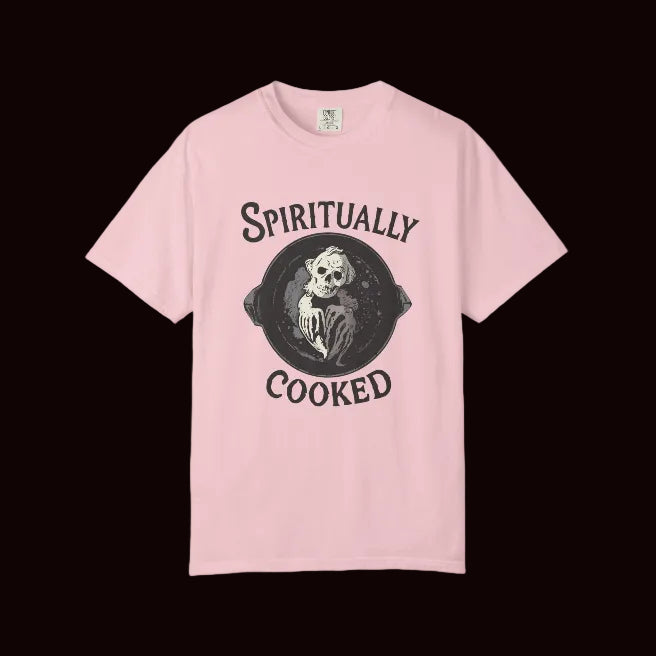 A light pink short-sleeve crewneck t-shirt featuring a black graphic print of a skeleton in a frying pan with the text 'SPIRITUALLY COOKED' on the front, displayed against a solid white background.