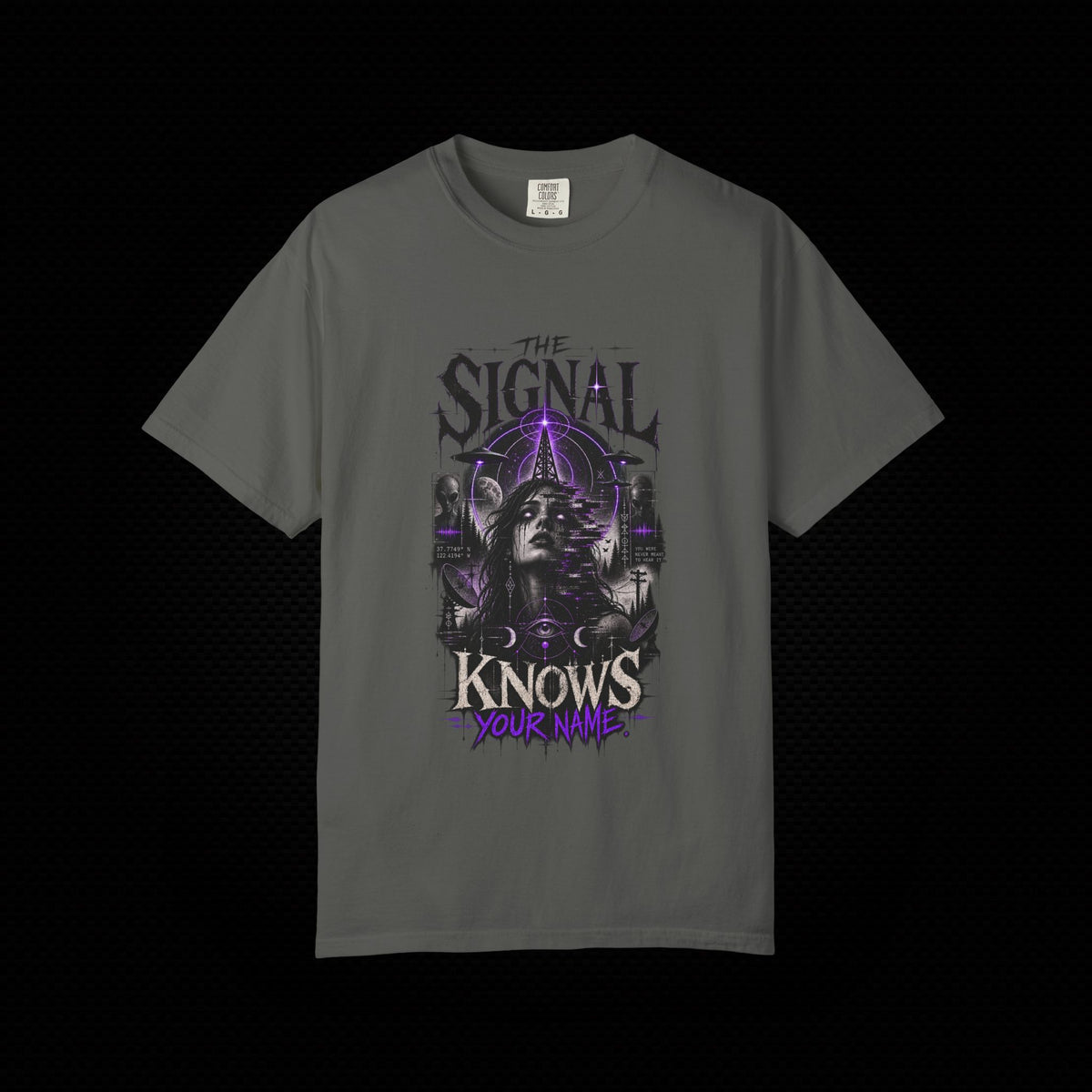 A dark gray short-sleeve t-shirt with a gothic-style graphic print featuring a woman's face, occult symbols, and the text 'THE SIGNAL KNOWS YOUR NAME' in purple and white, displayed against a black background.